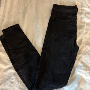 Svarta skinny jeans från Ambig - Svarta jeans från Ambig i skinny fit med klassisk femficksdesign och knappgylf. Jeansen har en smal passform och är tillverkade i stretchigt bomullsmaterial för extra komfort. Perfekta för dig som gillar en stilren och enkel look.