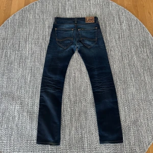 Mörkblå Lee jeans W31 L32 - Säljer ett par mörkblå jeans från Lee, modell Macky. Jeansen har klassisk femficksdesign, snygga kontrastsömmar och Lee-lapp bak i midjan. De är raka i modellen och tillverkade i slitstarkt denimtyg. Perfekta för dig som gillar en tidlös jeansstil.