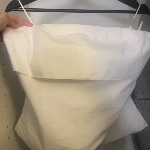 Vit axelbandslös tubtopp från Zara - Säljer en stilren vit tubtopp från Zara i storlek L. Toppen är axelbandslös med en bred kant upptill och dragkedja i ryggen för enkel påklädning. Perfekt att matcha med jeans eller kjol för en clean look.