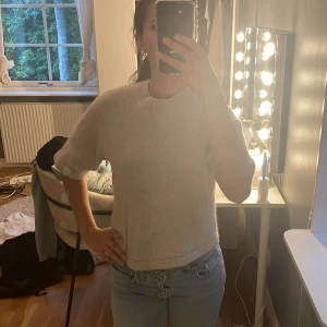 Beige stickad tröja med kort ärm - Mysig beige stickad tröja med korta ärmar och rund hals. Tröjan har en lite boxig passform och är perfekt för lager-på-lager. Den är enkel och stilren, vilket gör den lätt att matcha med jeans eller kjol.