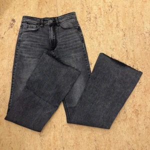 Gråa bootcut jeans med slits - Säljer ett par mörkgrå bootcut jeans med hög midja och råa kanter nertill. Jeansen har slits vid bensluten.