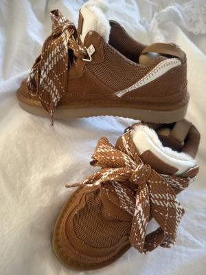 Bruna sneakers med fuskpäls och mönstrade snören - Säljer ett par bruna sneakers med breda, mönstrade snören i brunt och vitt. Skorna har mysig vit fuskpäls på insidan och detaljer i mocka och textil. Sulan är beige och har vågigt mönster undertill. Perfekta för höst och vinter när du vill vara både varm och snygg. Aldrig andvända, pris går att diskutera🤎🍂k0pia