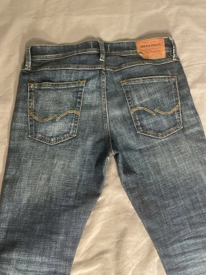 Blå jeans från Jack & Jones - Snygga blå jeans från Jack & Jones med slim passform och klassisk femficksdesign. Jeansen har slitningar och tvättad look, samt kontrastsömmar på bakfickorna. Materialet är jeans med en mjuk känsla och stretch för extra komfort.