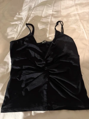 Svart shimmertopp🪩🌟 - Säljer en svart linnetopp från Bik Bok i storlek L. Toppen har tunna justerbara axelband och snygg snurrad detalj framtill. Materialet är syntet med en skimrande finish som ger en cool look. Perfekt att styla med jeans eller kjol för en trendig outfit.💿🪩🌟🌟