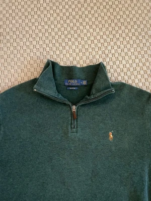 Grön half zip tröja från Polo Ralph Lauren - Snygg mörkgrön tröja från Polo Ralph Lauren med half zip och klassisk krage. Tröjan har lång ärm och är tillverkad i mjukt material med broderad logga på bröstet. Perfekt för dig som gillar stilren och enkel design.