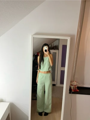 Grönt randigt wide set med resår - Säljer ett par ljusgröna byxor och topp med smala vita ränder. Byxorna har en relaxed wide fit, elastisk midja och är tillverkade i ett mjukt bomullsliknande material. Perfekt för chill dagar sommarn och våren och har en skön, loose passform. 