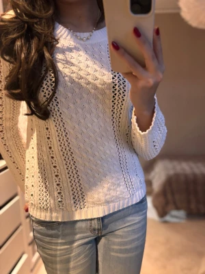 Vit stickad tröja med mönster - Säljer en vit stickad tröja med snyggt hålmönster och kabelstickade detaljer. Tröjan har rund hals och långa ärmar, perfekt att matcha med jeans. Den är mjuk och har ribbade muddar vid ärmslut och nederkant.