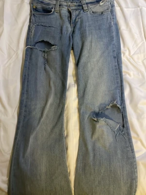 Cheap Monday ljusblå ripped jeans - Säljer ett par ljusblå jeans från Cheap Monday med slitna och trasiga detaljer på både lår och knä. Modellen har raka ben och klassisk femficksdesign. Jeansen är tillverkade i bomull och har en cool, vintage vibe med tydliga slitningar.