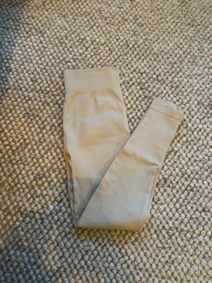 Beige ribbade leggings med hög midja - Säljer ett par beige ribbade träningstights med bred, hög midja. De är stretchiga och sitter tight💗 S/M