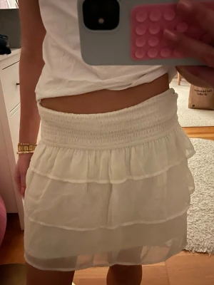 Vit volangkjol  - Säljer en söt vit kortkjol med flera volanger och resår i midjan. Jättefin till sommaren! Jättebra skick! Storlek xs!