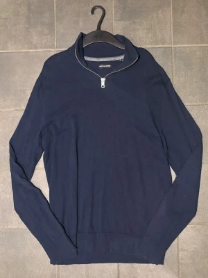 Marinblå half zip tröja Jack & Jones - Snygg marinblå långärmad tröja från Jack & Jones i storlek S. Tröjan har en stilren half zip-dragkedja vid kragen och är tillverkad i mjuk bomull. Perfekt för dig som gillar enkel och klassisk stil med en modern touch.