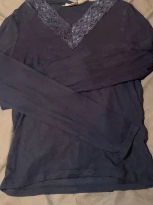 Mörkblå långärmad blus med spets - Säljer en mörkblå långärmad blus från Gina Tricot i storlek 146/152. Toppen har en snygg v-ringning med dekorativ spets i samma färg som ger en extra detalj. Materialet är mjukt och bekvämt, perfekt för dig som gillar stilrena plagg med lite extra touch.