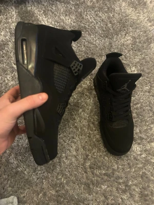 Jordan 4 black cats  - Säljer ett par helsvarta Jordan 4 black cats sneakers med snygga meshpaneler och klassisk Jumpman-logga på plösen. Skorna har snörning, platt sula och rund tå. Materialet är en mix av mocka och syntet, vilket ger en schysst och stilren look. Har använts 2 gånger. Fick dem i julklapp. Skriv vid eventuella frågor 
