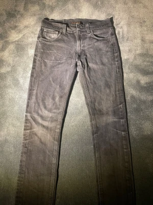 Svarta jeans från Nudie - Säljer ett par svarta skinny jeans från Nudie Jeans i storlek W29 L32. Jeansen har klassisk femficksdesign, svarta sömmar och Nudie Jeans logga på bakfickan. 