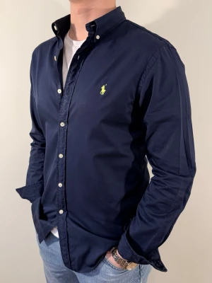 Mörkblå Ralph Lauren skjorta - En snygg polo skjorta som passar till alla tillställningar! Väldigt bra allround för festliga högtider som nyår eller vanliga sommarkvällar. Skjortan har inga deffekter🌟 Storlek👔: M Nypris💰: ca 1299 &