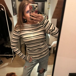 Randig långärmad topp i bomull från Gina - Säljer en vit långärmad topp med svarta ojämna horisontella ränder. Toppen har en klassisk rund halsringning och är i ett mjukt bomullsmaterial. Passformen är normal och toppen är perfekt att styla oavsett årstid . Aldrig använd! 