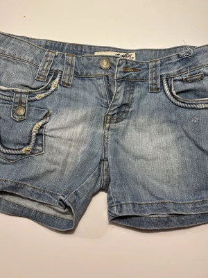 Gallop Jeans ljusblå denimshorts - Snygga ljusblå denimshorts från Gallop Jeans med coola detaljer som tvinnade kanter på fickorna och slitningar. Klassisk femficksmodell med knapp och dragkedja framtill. Perfekta för varma dagar och en avslappnad stil. Är begagnade men har själv aldrig använd och är för stora för mig.