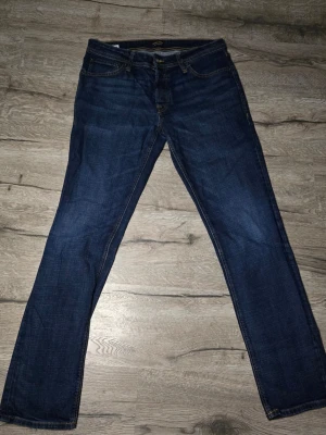 Jack & Jones Regular Clark jeans 33/34 - Mörkblå jeans från Jack & Jones i modellen Regular Clark. Klassisk femficksdesign med kontrastsömmar och rak passform. Tillverkade i slitstarkt bomullsmaterial, perfekta för dig som gillar en enkel och tidlös look.