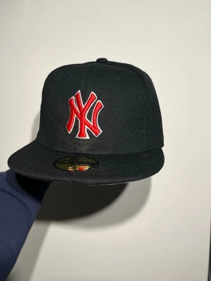 New York New Era Keps  - Bilderna visar en svart New Era keps med röd New York Yankees-logga, World Series-märke och broderad text, men ingen väst finns med.