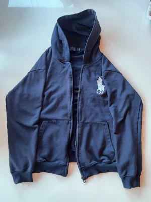 Ralph Lauren Big Pony Hoodie - En riktigt snygg ”Big Pony” Ralph Lauren hoodie i mörkblå färg. Passar till det mesta. Detaljer som en stor häst och en 3a på en av armarna. DMa om du har frågor. Pris är inte satt i sten.