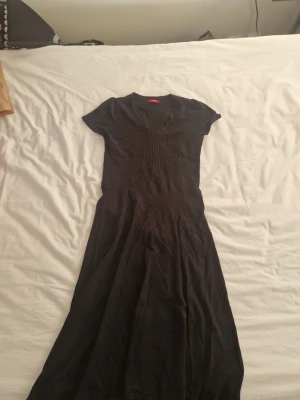 Svart långklänning från LC Waikiki - Svart långklänning från LC Waikiki i storlek M. Klänningen har korta ärmar, v-ringad hals och ribbade detaljer vid bröstet. Materialet känns mjukt och bekvämt, perfekt för dig som gillar enkel och stilren design.