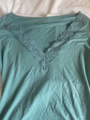 Turkos långärmad topp med spets - Säljer en turkos långärmad topp med v-ringning som är dekorerad med spetsdetaljer. Toppen har en mjuk och skön känsla, perfekt för dig som gillar stilrena plagg med en liten twist. Passar dig som vill ha något enkelt men ändå med lite extra. bara använd 2 gånger.