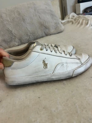 Vita Polo Ralph Lauren sneakers med glitter - Ge gärna prisförslag❗️Säljer ett par vita sneakers från Polo Ralph Lauren med guldfärgade glittriga detaljer på hälen. Skorna är väl använda, som man kan se på hålet i sulan. De är även smutsiga eftersom jag inte hunnit tvätta dem. Men smutsen går att få bort så man får tillbaka den vita färgen💖annars funkar de bra❗️