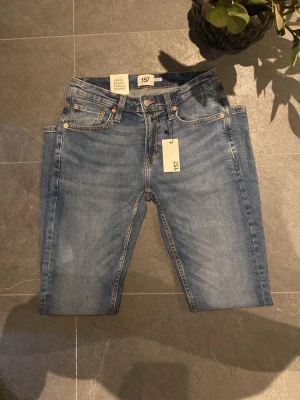 Blå skinny jeans från 157 - Snygga blå skinny jeans från 157 med klassisk femficksdesign och guldfärgade nitar. Jeansen har en smal passform, normal midja och är tillverkade i mjukt denim-material. Perfekta för dig som gillar en stilren och enkel look.