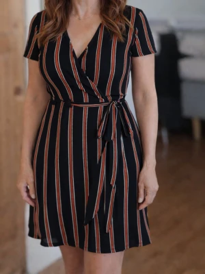 Svart kort omlottklänning med ränder - Snygg svart omlottklänning från H&M med vertikala röda, vita och beige ränder. Klänningen har korta ärmar, v-ringning och knytband i midjan. Materialet är mjukt och stretchigt, 97% polyester och 3% elastan. Perfekt för dig som gillar en trendig och bekväm look.