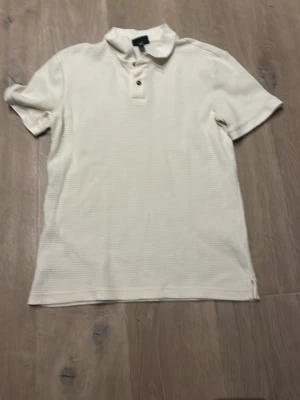 Vit slim fit polotopp från H&M - Säljer en vit polotopp från H&M i slim fit-modell. Toppen har korta ärmar, krage och två knappar framtill. Materialet är mjukt och har en diskret ribbad struktur som ger en cool känsla. Perfekt för dig som gillar stilrena och enkla plagg.