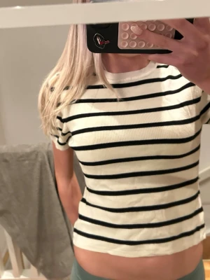 Vit och svart randig t-shirt - Snygg vit t-shirt med svarta horisontella ränder och rund hals. Modellen är kortärmad och har en slim passform som sitter nära kroppen. Perfekt för dig som gillar en enkel men stilren look. Materialet känns mjukt och bekvämt mot huden. Skulle säga att det är storlek S