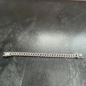 Glittrig silverfärgad kedjearmband - Säljer ett chunky kedjearmband i silverfärg med glittrande stenar på varje länk och ett lås som också är täckt av stenar. Armbandet är 20 cm långt! Armbandet har en rejäl känsla, vid intresse bara att höra av sig. 