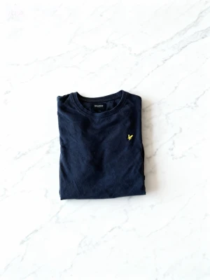 Lyle & Scott T-shirt - Svart Lyle & Scott T-shirt – Stilren och Ikonisk! Uppgradera garderoben med denna klassiska Lyle & Scott t-shirt i svart. Mjuk, skön bomull och den ikoniska gyllene örnloggan på bröstet ger en tidlös och stilfull look. Perfekt att bära till allt – från jeans till shorts. Storlek: M  Skick: Mycket bra  Material: 100% bomull En enkel, men ändå stilfull t-shirt som aldrig går ur modet – perfekt för dig som vill ha både komfort och klass!