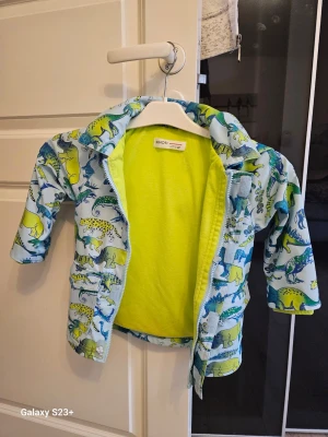 Färgglad vindjacka med djur från Minoti - Säljer en cool vindjacka från Minoti med huva och dragkedja. Jackan har ett färgstarkt djurmönster i blått, grönt och gult på ljus bakgrund samt mjukt gult foder. Perfekt för dig som gillar roliga prints och vill sticka ut.