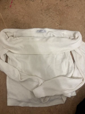 Vit offshoulder tröja från Stradivarius - Säljer en snygg vit ribbad offshoulder tröja från Stradivarius i storlek S. Tröjan har långa ärmar och är tillverkad i mjuk bomullsmix, perfekt för dig som gillar stilrena och trendiga plagg. Passar dig som vill ha en fräsch och modern look.