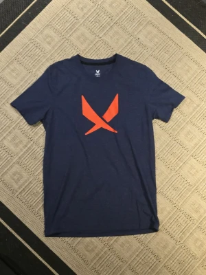 Blå SOC t-shirt med orange tryck - Säljer en mörkblå t-shirt från SOC i storlek S med ett stort orange tryck på bröstet. T-shirten har rund hals och korta ärmar, tillverkad i mjuk bomull/polyesterblandning som andas bra. Perfekt för dig som gillar sportig och clean stil.