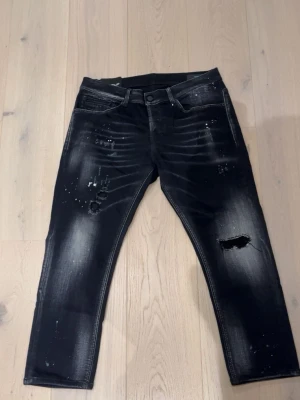 Dondup jeans - Säljer ett par svarta jeans från Dondup med coola slitningar och färgstänk på både fram- och baksida. Jeansen har en skinny passform och klassisk femficksdesign. Materialet är jeans med stretch för extra komfort. Perfekt för dig som gillar en edgy streetstil.
