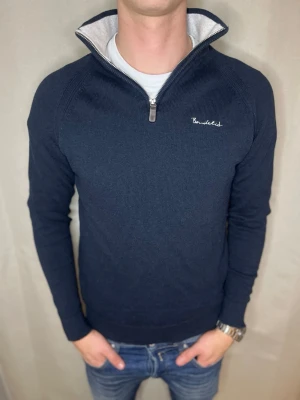 Marinblå stickad tröja från Bondelid - Säljer en marinblå stickad tröja från Bondelid med halv dragkedja och vit broderad logga på bröstet. Tröjan har hög krage med ljusgrå insida och långa ärmar. Perfekt för dig som gillar klassisk och stilren look. Skick 7/10. Vi kan gå ner i pris vid snabb och smidig affär. // Studio II resell. 