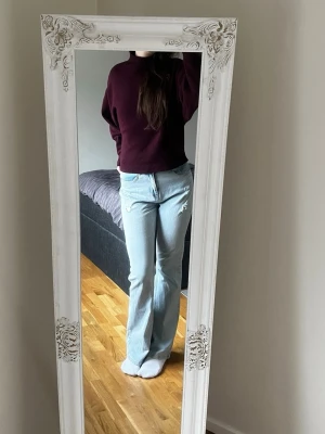 Ljusblå bootcut jeans - Säljer ett par ljusblå jeans med bootcut-snitt och klassisk femficksdesign. Jeansen har en hög midja och är tillverkade i mjukt denimtyg. De har diskreta slitningar framtill för en cool look och raka ben som breddas nedtill.