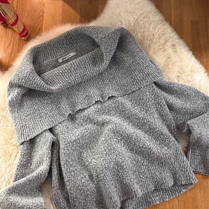 Grå stickad tröja Gina Tricot - Säljer en grå stickad tröja från Gina Tricot i storlek S. Tröjan har en bred, ribbad krage som går över axlarna och ger en snygg offshoulder-look. Materialet är mjukt och mysigt, perfekt för kyliga dagar. Passformen är loose och ärmarna är långärmade.