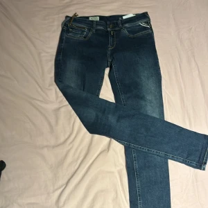 Replay Luz jeans blå storlek 28/30 - Snygga Replay Luz jeans i klassisk blå tvätt med kontrastsömmar och fem fickor. Modellen har smal passform och raka ben, midja med knapp och dragkedja. Perfekt för dig som gillar stilrena och tidlösa jeans.
