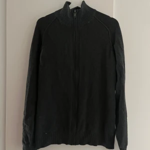 Svart kofta från Angelo Litrico - Svart kofta från Angelo Litrico med hel dragkedja framtill och ribbad hög krage. Tröjan har långa ärmar och ribbade muddar vid ärmslut och nederkant. Perfekt för lager-på-lager och enkel att matcha med det mesta.