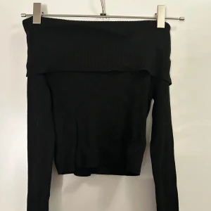 Svart ribbad offshoulder topp - Säljer en svart ribbad offshoulder topp med långa ärmar. Toppen har en bred kant upptill som ger en snygg offshoulder-look och är tillverkad i ett stretchigt, ribbat material som sitter tight och bekvämt. Perfekt för dig som gillar stilrena och trendiga plagg.
