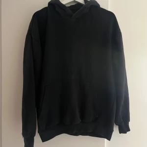 Svart hoodie från Bershka loose fit - Svart hoodie från Bershka i loose fit-modell. Klassisk design med huva och stor magficka framtill. Perfekt för dig som gillar en avslappnad och enkel stil. Mjuk insida och ribbade muddar vid ärmslut och nederkant.