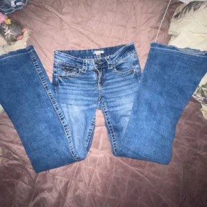 Blå bootcut jeans från Gina Tricot - Snygga blå jeans från Gina Tricot i storlek 158. Modellen har bootcut-ben och klassisk femficksdesign med knappar på bakfickorna. Jeansen är i denim med en lätt tvättad look och har normal passform. Perfekta för dig som gillar en tidlös stil.