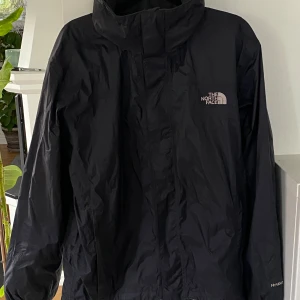 Svart vindjacka från The North Face! Nyskick!  - Svart vindjacka från The North Face med HyVent-teknologi. Jackan har huva, dragkedja framtill och meshfoder på insidan. Klassisk logga på bröstet och ryggen. Endast använd 2 gånger! Så är som ny!! 