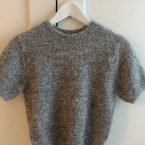 Grå stickad kortärmad tröja - Mysig grå stickad tröja med korta ärmar och rund hals. Perfekt för lager-på-lager och passar till både jeans och kjol. Tröjan har en enkel och stilren look med ribbade kanter vid hals och midja. köpt 2024 men aldrig använt!