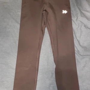 Brun/Rosa leggings från 157 i storlek S - Snygga brun/rosa  leggings från 157 i storlek small. De är stretchiga och har en tight passform, perfekta för träning eller chill. Materialet är mjukt och följsamt syntet, med en diskret logga på höften. Enkla att matcha med oversized hoodie eller crop top.