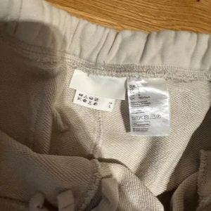 Beige shorts med resårmidja, storlek L - Säljer ett par stilrena beige shorts i storlek L med elastisk midja och snörning. De är tillverkade i mjuk bomull och har en enkel, rak passform som går ner till strax ovanför knäna. Perfekta för chill dagar eller när du vill ha en clean look.