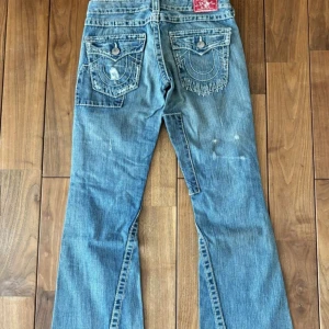 True Religion patchwork bootcut jeans - Säljer ett par blå bootcut jeans från True Religion med patchwork-detaljer och slitningar. Jeansen har markerade bakfickor med vita sömmar och klassisk röd True Religion-label. Tillverkade i USA och i klassisk denim med coola kontrastsömmar.